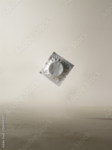 A minimalist product-style composition featuring a floating condom packet against a soft neutral background, emphasizing contraception, sexual health, protection, and modern wellness concepts.