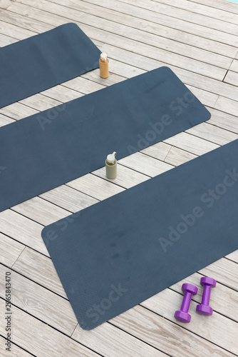 Central slate-blue exercise mat is lying diagonally on wood deck, with bottles and purple weights