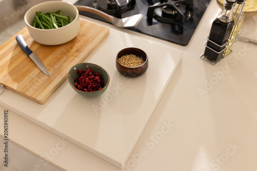 Wooden board, blue knife, green beans, pomegranate and pine nuts sitting near gas stove on counter