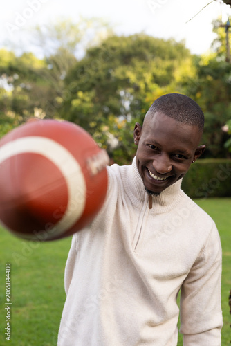 Adult man leaning and holding blurred football near camera on lawn in quarter-zip, studs, nose ring