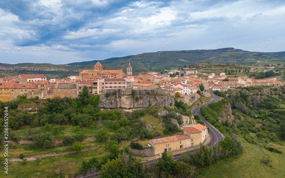 Fototapeta premium Aerial view of Cantavieja medieval town perched on limestone cliff with church towers, terracotta rooftops and winding road, Maestrazgo, Teruel, Aragon, Spain