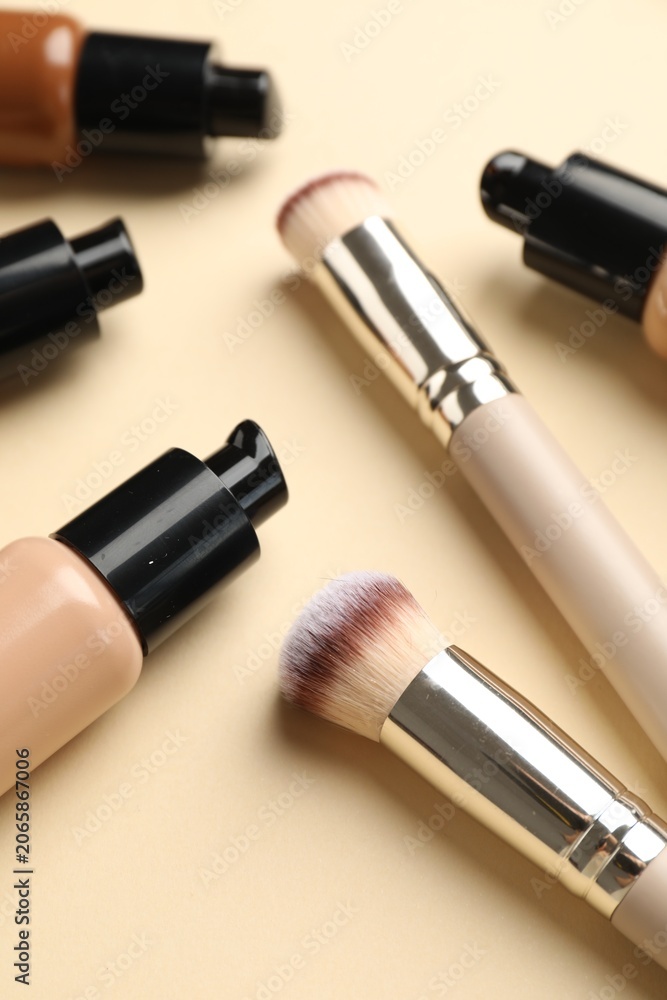 Obraz premium Makeup brushes and bottles of foundation on beige background, closeup