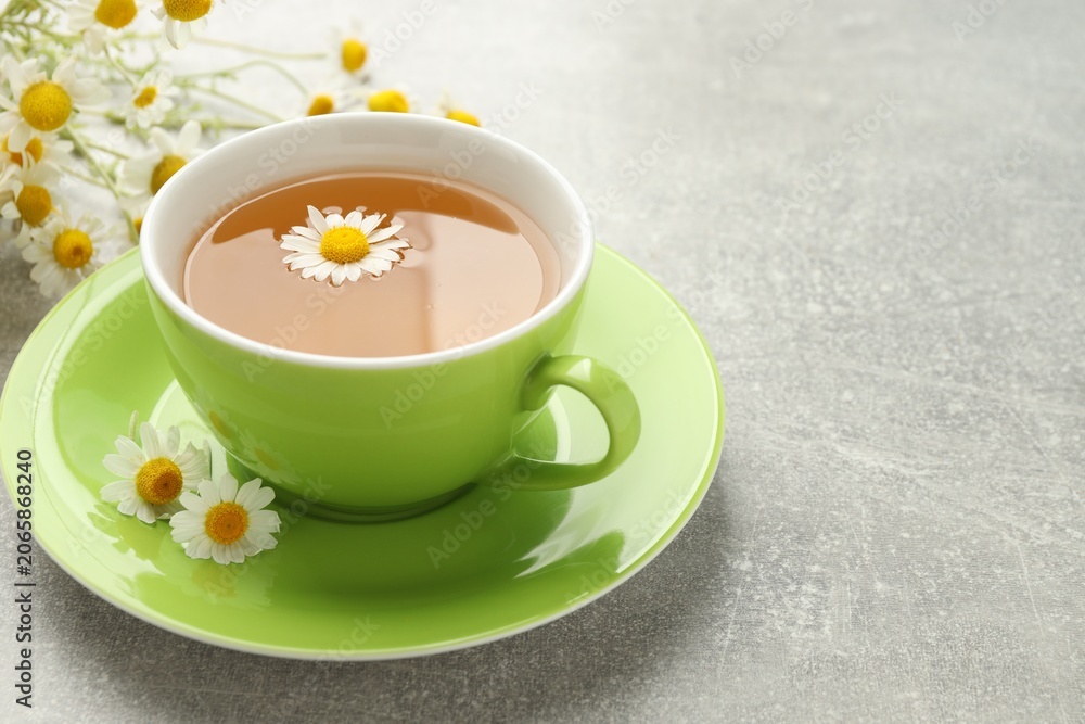 Obraz premium Cup of aromatic chamomile tea and flowers on light grey table, closeup. Space for text