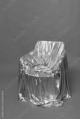 Eerie empty armchair draped in silver evoking a psychological void.