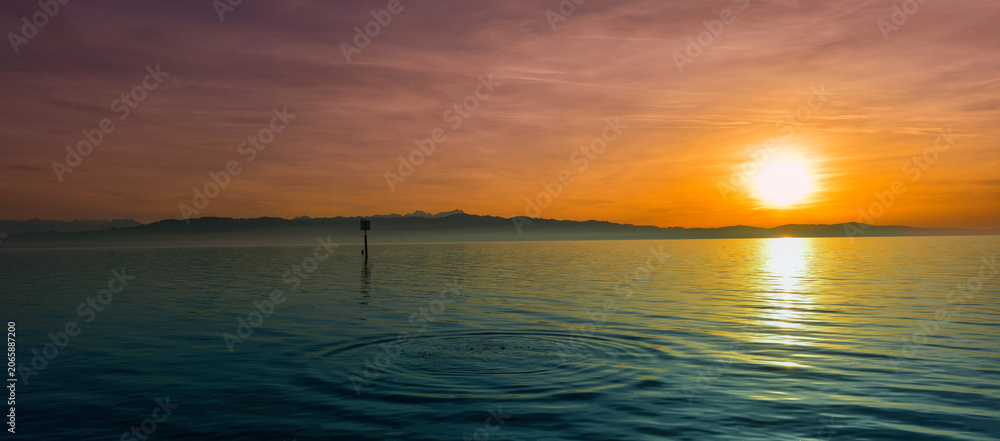 Fototapeta premium Malerischer Sonnenuntergang in Wasserburg am Bodensee mit Blick auf das Alpenpanorama und Wasserringen im Vordergrund