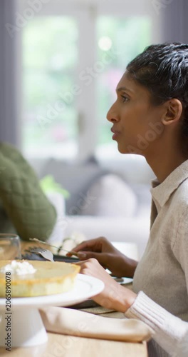 Vertical video: Two friends sitting at table while talking, woman cutting pie with fork, copy space