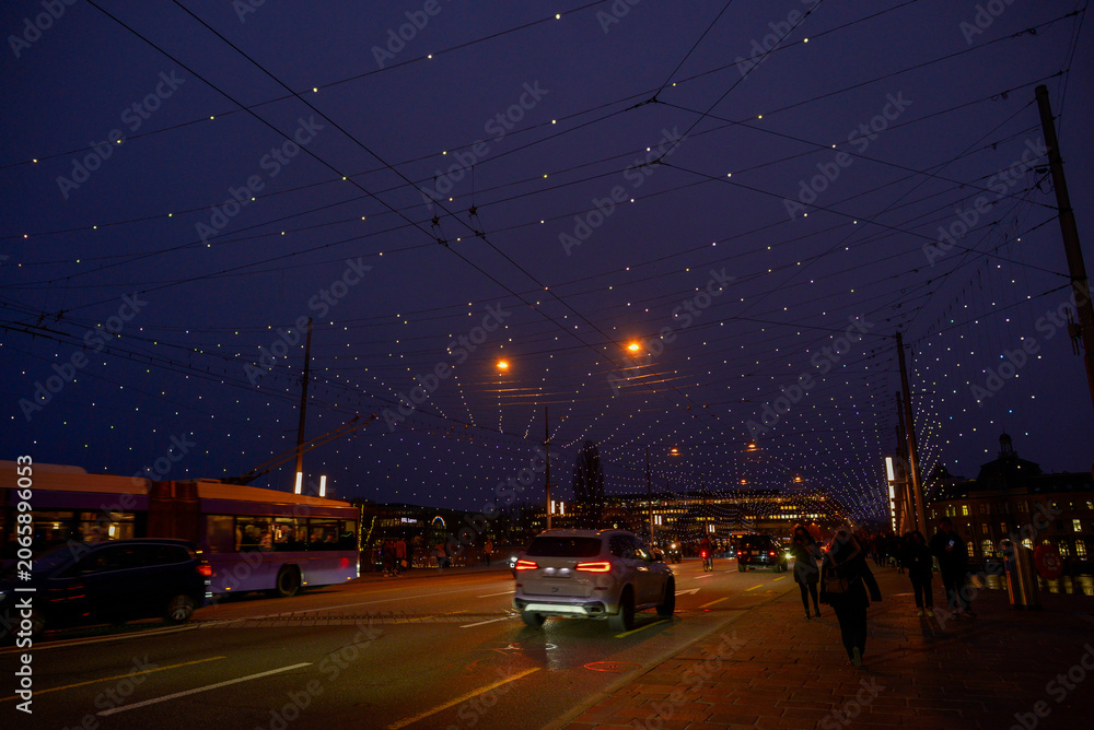 Fototapeta premium Weihnachtsbeleuchtung auf der Seebrücke in Luzern mit Verkehr und Passanten bei Dämmerung