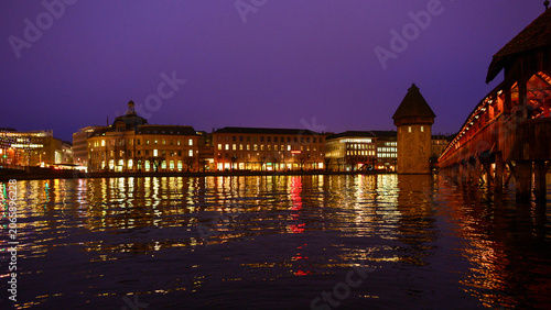 Tableau sur toile Beleuchtete Kapellbrücke mit Wasserturm und Uferpromenade in Luzern bei nächtlic