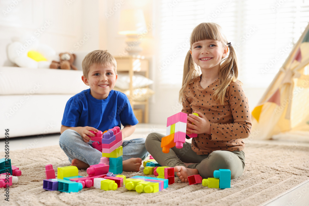 Naklejka premium Little kids playing with colorful blocks on floor at home