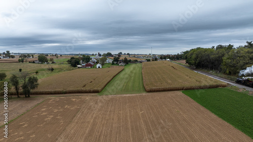 Cornfields line the land with a few houses visible in the distance. A railway track runs along the edge of the fields as clouds fill the sky. The scene shows rural life on a fall day.