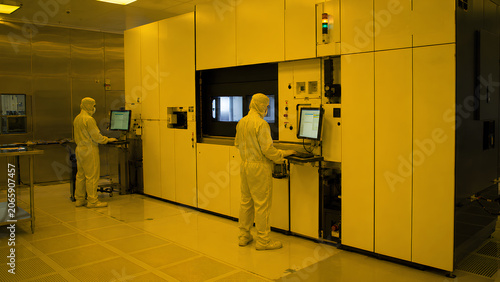 workers in cleanroom suits operating semiconductor lithography equipment in fabrication facility
