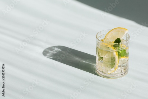 Minimalist high-angle shot of a classic gin and tonic cocktail casting a long shadow on a white surface