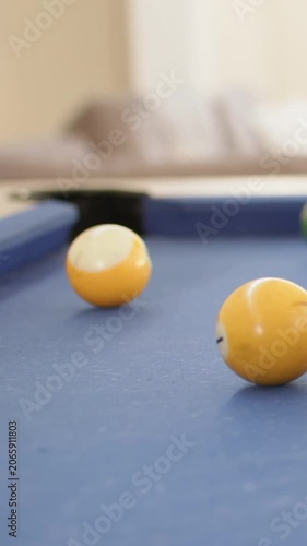 Vertical video: Rolling yellow solids, striped and green balls moving on blue-felt pool after hit