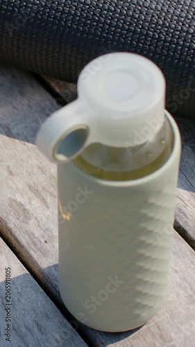 Vertical video: Tilting camera revealing reusable bottle with clear cap loop and droplets on deck