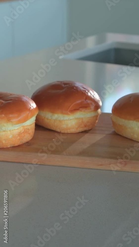 Vertical video: Shifting camera focusing front right bun on glossy counter, cutting board and sink