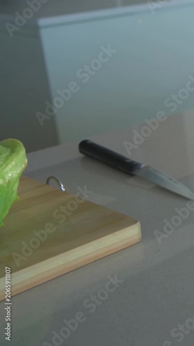 Vertical video: Panning camera showing lettuce wedge on board on counter with onion tomatoes knife