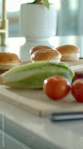 Vertical video: Slow panning camera showing lettuce, tomatoes and buns on board for sandwich prep