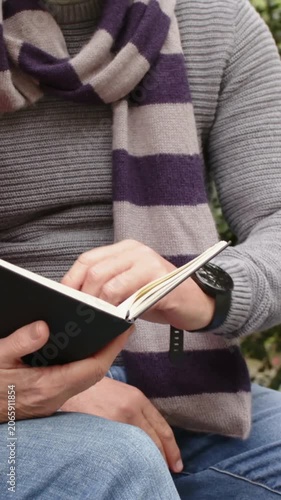 Vertical video: Opening notebook man in sweater pointing at pages and reading on bench