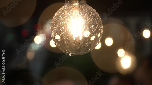 Raindrops falling on a garland bulb, the wind moves it, close-up shot, aesthetic video, decor. blurred raindrops, bokeh of warm incandescent lights