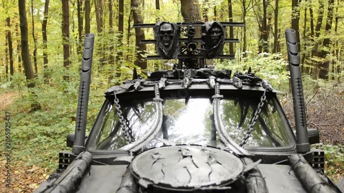 Menacing vibe, spiked vehicle, intimidating decor. Menacing vehicle with heavy armor, skull embellishments, and chains stands in forest, exuding post-apocalyptic atmosphere.