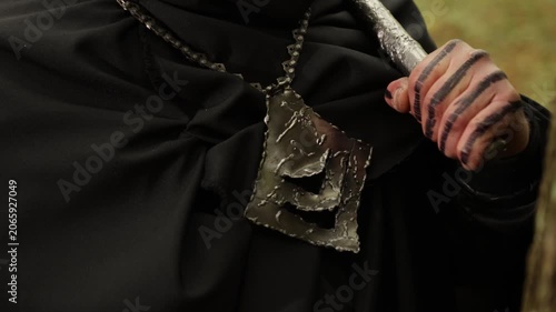 Weapon handle, Pendant chain, Metal jewelry. Rugged metal pendant on chain, with hand clutching weapon handle against black cloak.