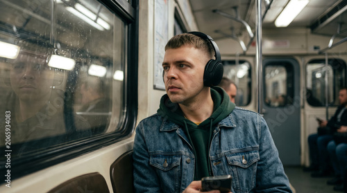 Young caucasian man commuting by subway train with wireless headphones and smartphone, listening to music during urban city travel