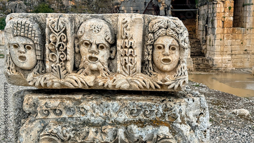 Fotografie Ancient carved stone theater masks in weathered ruins with soft natural light, p