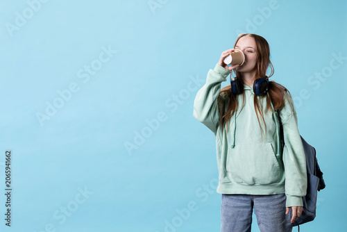 Fotografie Young girl with backpack feeling tired, drinking coffee to wake up