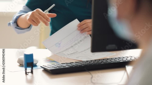 A doctor is typing on a document at a desk, using a computer in a well-lit office during the day
