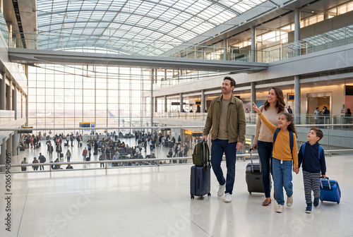 Happy family walking with luggage through large airport terminal before vacation