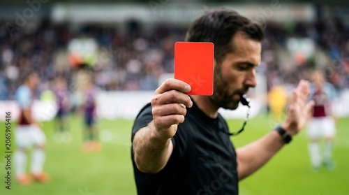 Referee holding up a red card during a soccer match with players in background