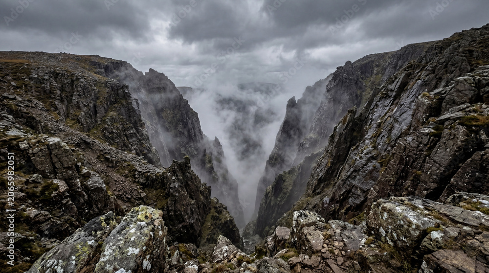 Obraz premium Looking Down Into Steep Rocky Ravine With Swirling Mist Between Sharp Stone Walls Mountain Landscape