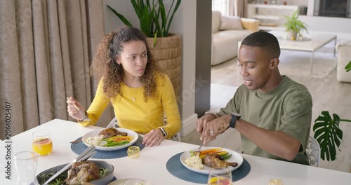Diverse couple starting dinner at table, cutting and tasting roasted meat with fork and knife