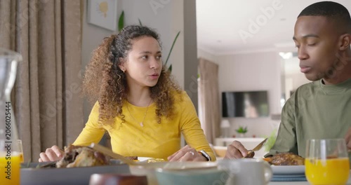Couple sharing meal at dining table, woman in yellow cutting with fork and knife, man eating