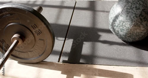Camera is panning right up, revealing 10kg plate, medicine ball on mat near window showing training