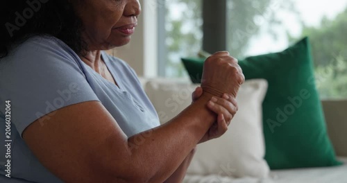 Senior African American woman on sofa in blue feeling wrist pain, rubbing left wrist, copy space