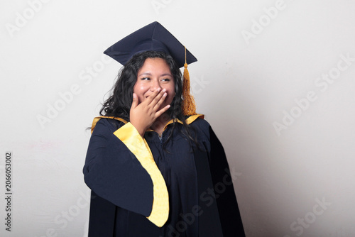 Young, dark-haired Latina woman dressed in a cap and gown is happy and excited to celebrate her graduation