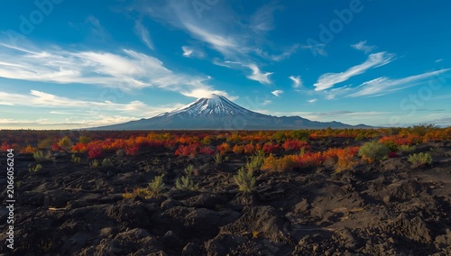 A breathtaking view of a snow-capped mountain, its peak partially shrouded in clouds against a clear blue sky.