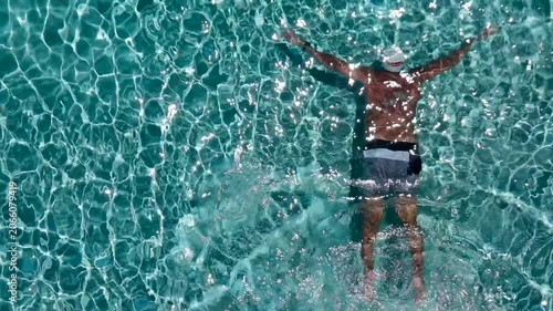 Aerial overhead view of a man swimming underwater in a clear turquoise swimming pool with bright shimmering sun reflections