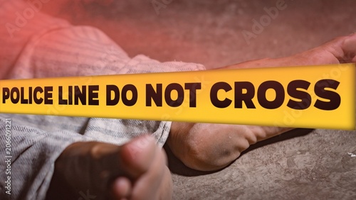 Crime scene concept with a dead body lying on the ground covered by a cloth, behind a yellow tape with the text POLICE LINE DO NOT CROSS.