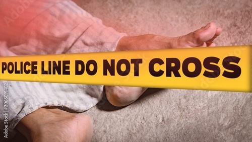 Crime scene concept with a dead body lying on the ground covered by a cloth, behind a yellow tape with the text POLICE LINE DO NOT CROSS.