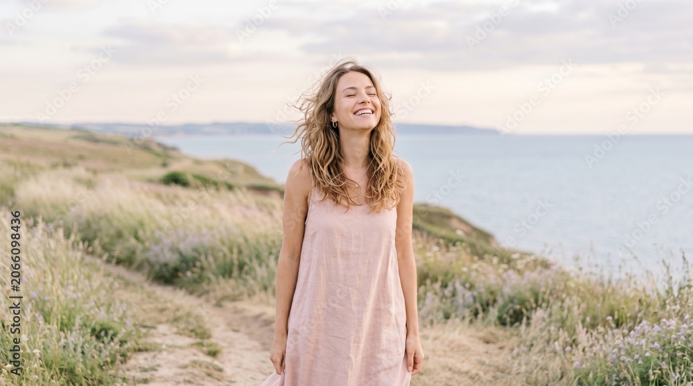 Obraz premium Young woman laughing joyfully on a coastal path with ocean in background