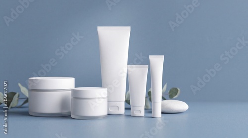 Group of white and blank, unbranded cosmetic cream jars and tubes on blue background. Skin care product presentation. Elegant mockup. Skincare, beauty and spa. Jar, tube with copy space. 3D rendering.