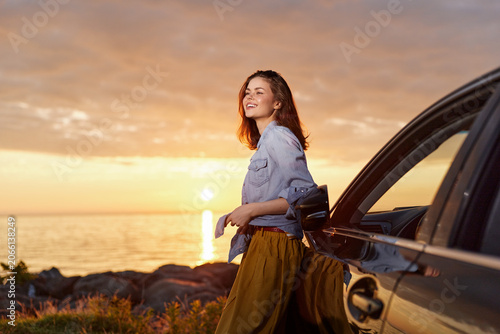 Foto Cheerful woman outdoors by a car at sunset, wearing a denim jacket and flowing s