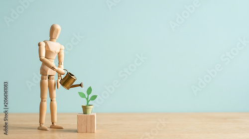 Business growth analysis and employee evaluation concept with wooden mannequin watering a growing plant for mid-year performance review presentation banner with copy space