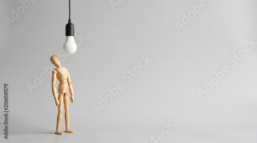 Business growth analysis and strategic employee evaluation concept with a wooden mannequin looking up at a light bulb featuring copy space for a mid-year performance reviews presentation banner.