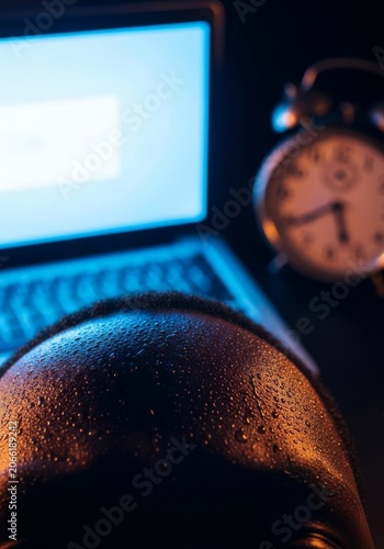 Dark skin with beads of sweat near a glowing laptop screen and ticking clock, symbolizing the intense pressure of a looming work deadline, lighting, lifestyle, computer