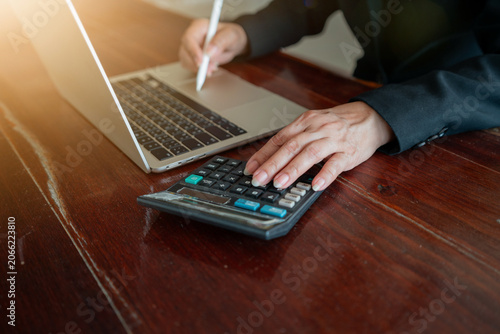 Businessman working with laptop and calculator on wooden desk with lens flare.