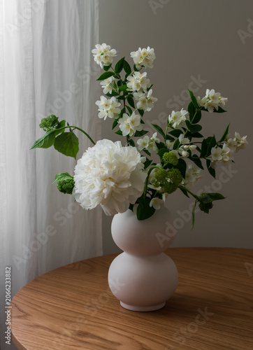 Bouquet of jasmine and white peonies in a ceramic vase on a wooden table in the living room
