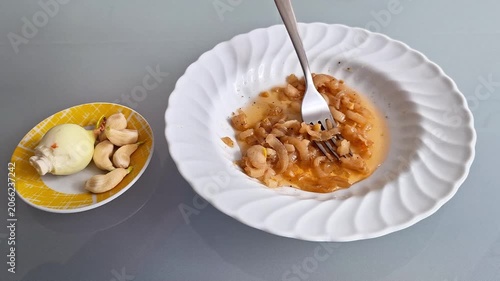 A simple meal preparation scene featuring sliced onions mixed with sauce on a white plate, with fresh onion and garlic cloves served on a small side dish. Casual home cooking concept